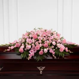 Pink floral casket spray on a dark wood casket