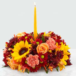 Floral centerpiece with a tall yellow candle and mixed red, yellow, and peach blooms