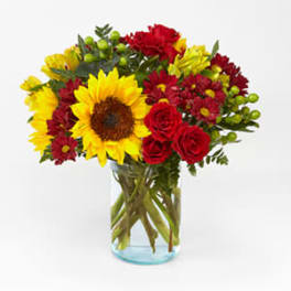 Bouquet of sunflowers, red roses, and red daisies in a glass vase