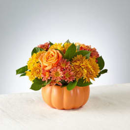 Orange and yellow flower arrangement in a pumpkin-shaped container