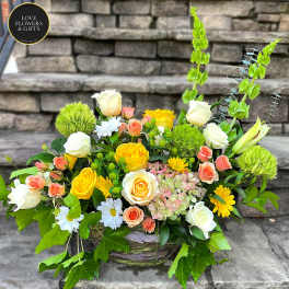 Low arrangement of yellow and white roses with peach roses and daisies in a rustic bowl.
