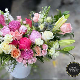Mixed arrangement of pink peonies, roses, and lilies in a white ceramic vase