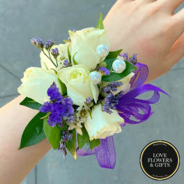 White rose wrist corsage with purple flowers, pearls, and ribbon on a person's arm