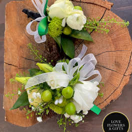 Pair of white and green floral boutonnieres with ribbons displayed on a rustic wood slice