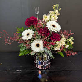 Compact arrangement of red and white flowers in an iridescent mosaic glass vase