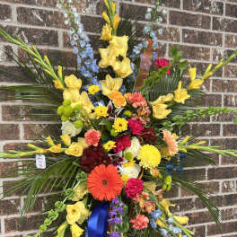 Large standing floral spray with yellow, blue, and mixed blooms on a brick wall