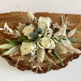 Cream roses with dried grasses in a compact arrangement on a rustic wood slice