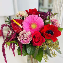 Bright bouquet of pink gerbera, red rose, carnations and anthurium in a clear glass vase