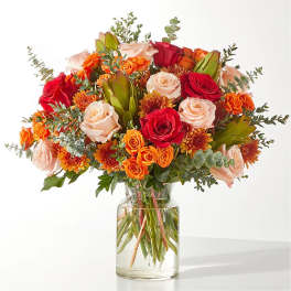 Bouquet of red, peach, and orange roses in a clear glass vase