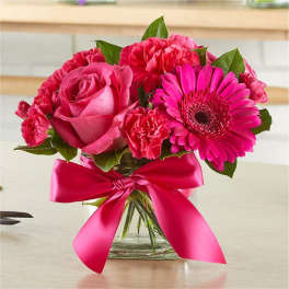 Small hot pink rose, gerbera daisy, and carnation arrangement in a glass cube with pink ribbon bow