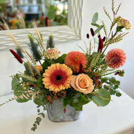 Low orange and peach flower arrangement with gerbera daisy, dahlias, and roses in a gray rectangular vase