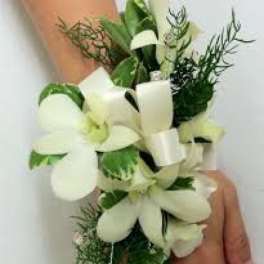 White floral wrist corsage with green foliage on a person's wrist