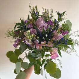 Handheld bouquet of lavender roses and purple flowers with trailing greenery