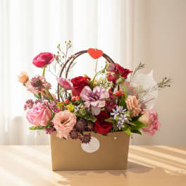 Mixed pink and red flower arrangement in a brown gift box with a heart handle