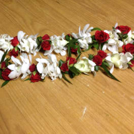 Red and white floral lei with ribbon on a wooden surface