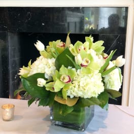 White and green floral arrangement in a square glass vase