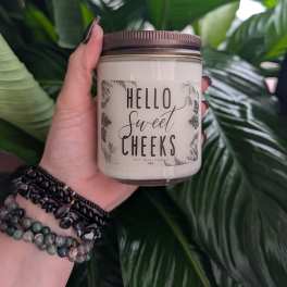 Hand holding a soy wax candle jar in front of large green leaves