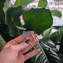 Hand holding a gold floral pick in front of large green leaves