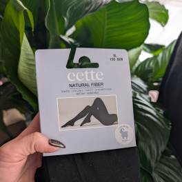Hand holding packaged black tights in front of green leaves