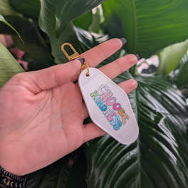 Hand holding a keychain tag in front of large green leaves