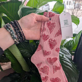 Pink socks with red hearts held in front of large green leaves