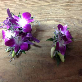 Two purple orchid corsages with ribbon accents on a wooden surface