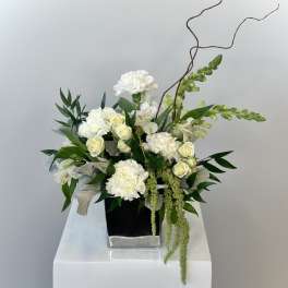 White carnations and roses arranged in a black square vase