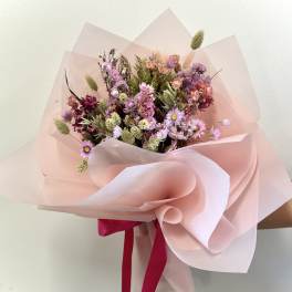Hand-tied bouquet of pink and purple dried flowers wrapped in pale pink paper