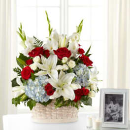 Basket arrangement of red roses, white lilies, and blue hydrangeas