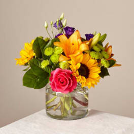Bouquet of sunflowers, roses, and purple blooms in a glass vase