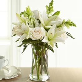White lilies and roses arranged in a clear glass vase