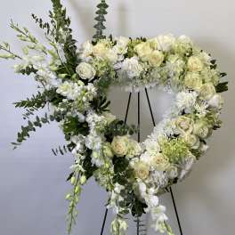 Heart-shaped white floral wreath on a black stand