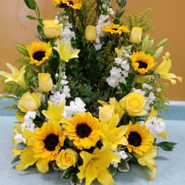 Yellow sunflowers, roses, and lilies arranged in a tall display