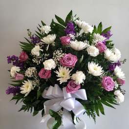 Bouquet of pink roses, white daisies, and purple flowers with a white ribbon