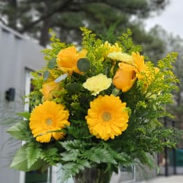 Yellow flowers and roses arranged in a clear glass vase.