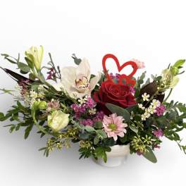 Mixed floral arrangement with a red rose and heart pick in a white container