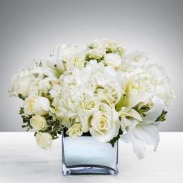 White roses and calla lilies arranged in a square glass vase.