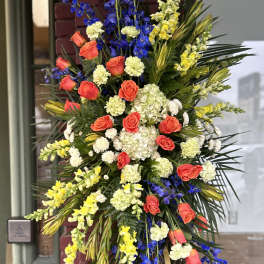 Standing floral spray with red roses, blue delphinium, and yellow snapdragons