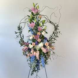 Tall floral spray with pink lilies, roses, and blue flowers on a stand
