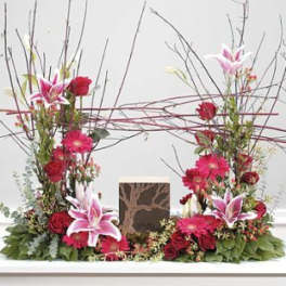 Tall floral arrangement with pink lilies and red flowers around a framed card