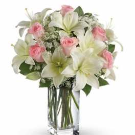 Tall glass vase arrangement with white lilies, pink roses, and delicate white filler flowers.