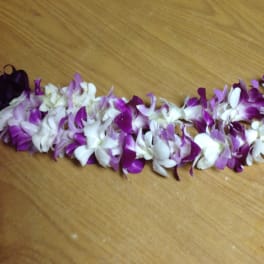 Purple and white orchid lei laid on a wooden surface