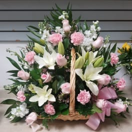 Basket arrangement of pink roses, white lilies, and carnations with a pink ribbon