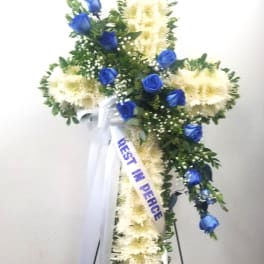 Standing floral cross with blue roses and white flowers on an easel