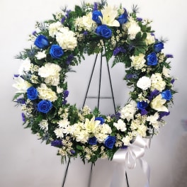Blue and white floral wreath on a black stand with a white ribbon