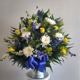 White and yellow floral arrangement with blue ribbon in a white vase