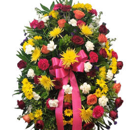 Large standing floral wreath with roses, chrysanthemums, and a pink ribbon
