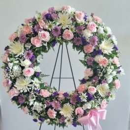 Pastel floral wreath on a black stand with a pink ribbon