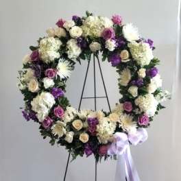 Circular floral wreath on a stand with purple, white, and cream flowers