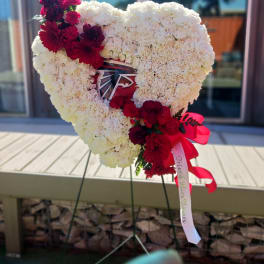 Heart-shaped white floral tribute with red flowers and ribbon